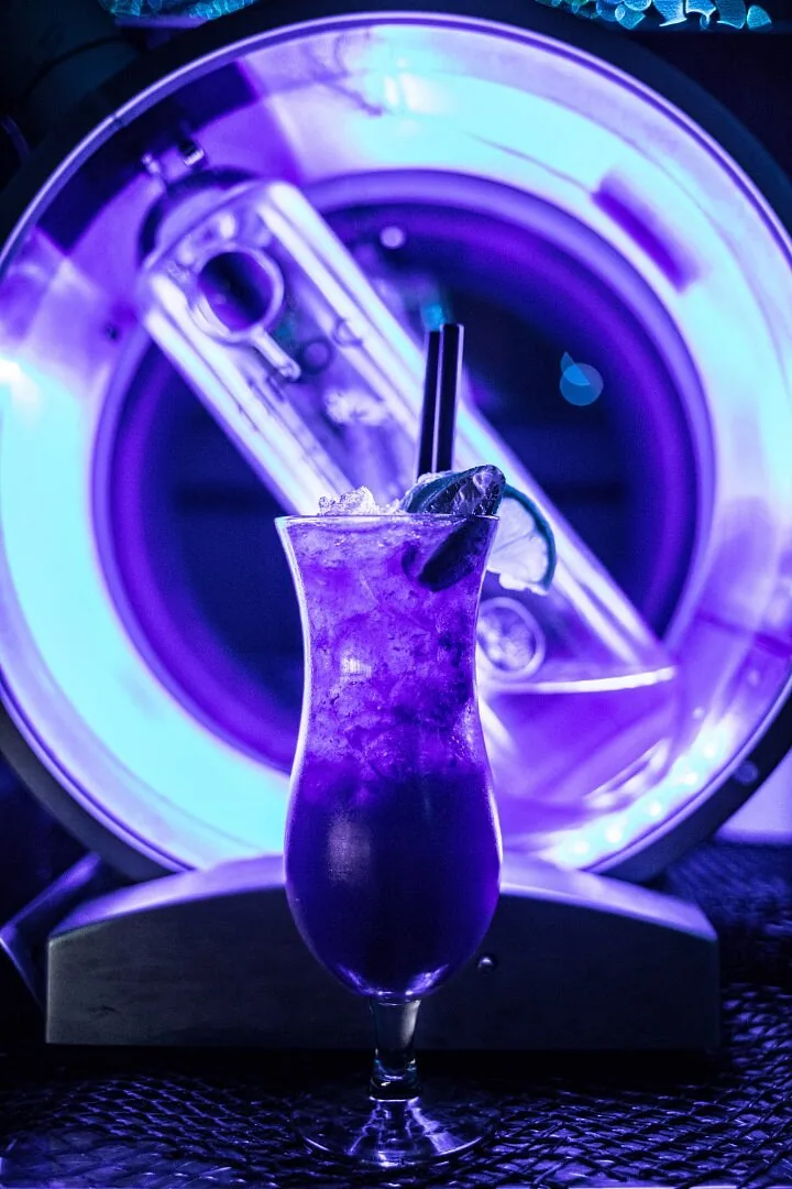 Violet signature cocktail glowing in front of a neon ring