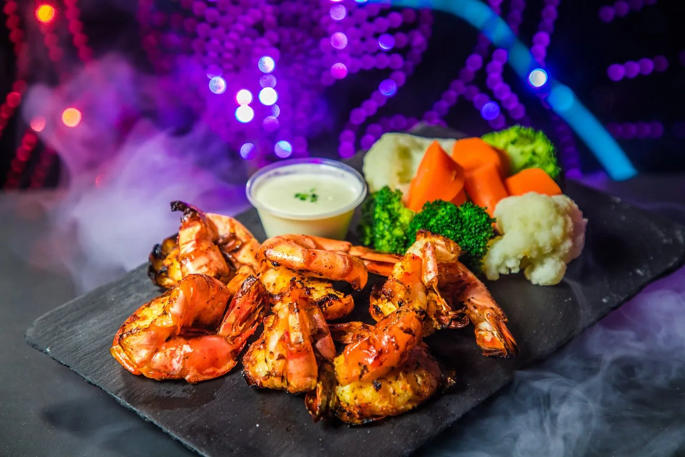 Grilled prawns with vegetables and dip on a slate