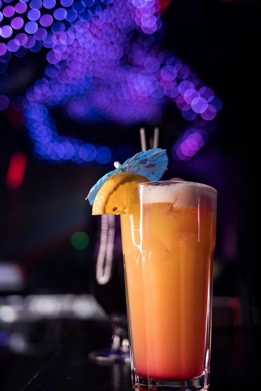 Orange and red sunset-style long drink with a paper umbrella