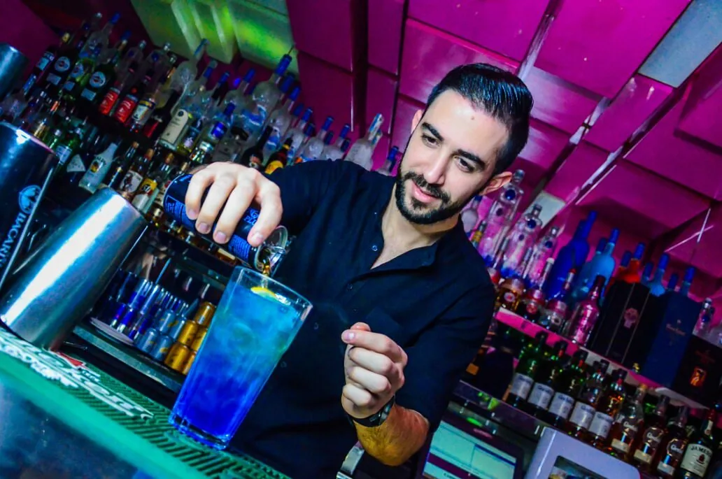 Smiling bartender mixing a blue cocktail at the bar