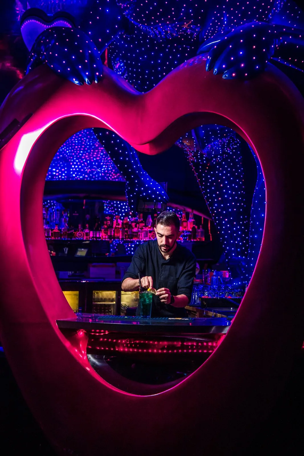 Bartender framed by the pink heart sculpture at the Chameleon Club Dubai bar